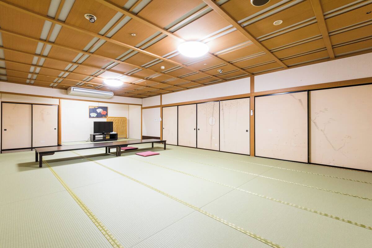 A tatami mat room with a wooden ceiling, a bench, and a television.