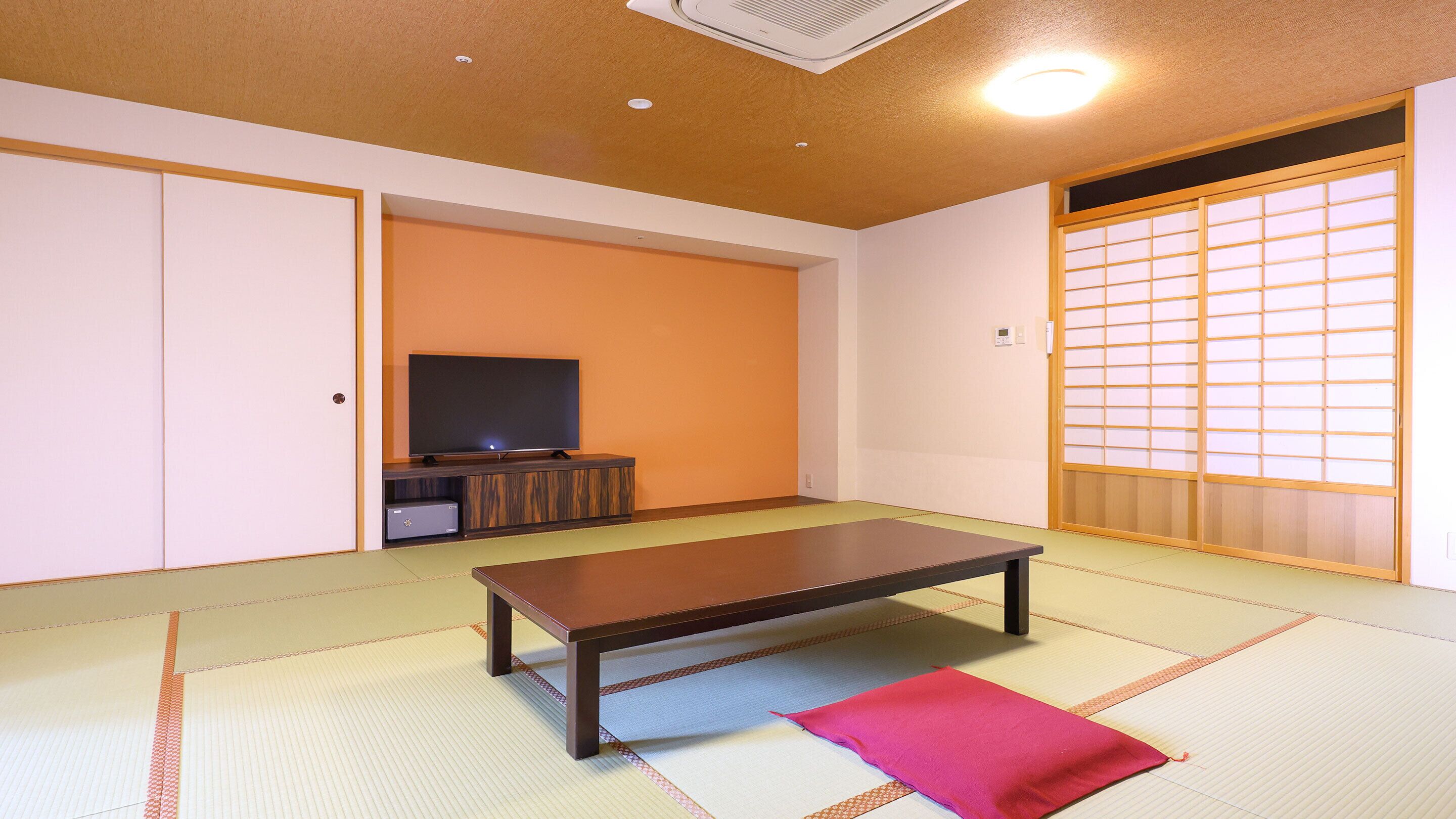Une pièce avec un sol recouvert de tatamis, un téléviseur posé sur un meuble, une porte coulissante dotée de panneaux shoji et un futon sur le sol.