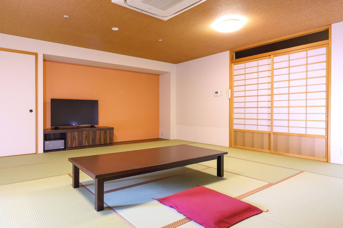 A room with tatami flooring, a television on a stand, a sliding door with shoji screens, and a futon on the floor.