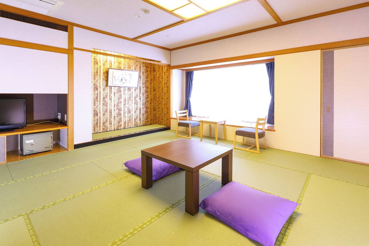 A traditional Japanese room with tatami flooring, a low table with cushions, a television, and a sliding door.