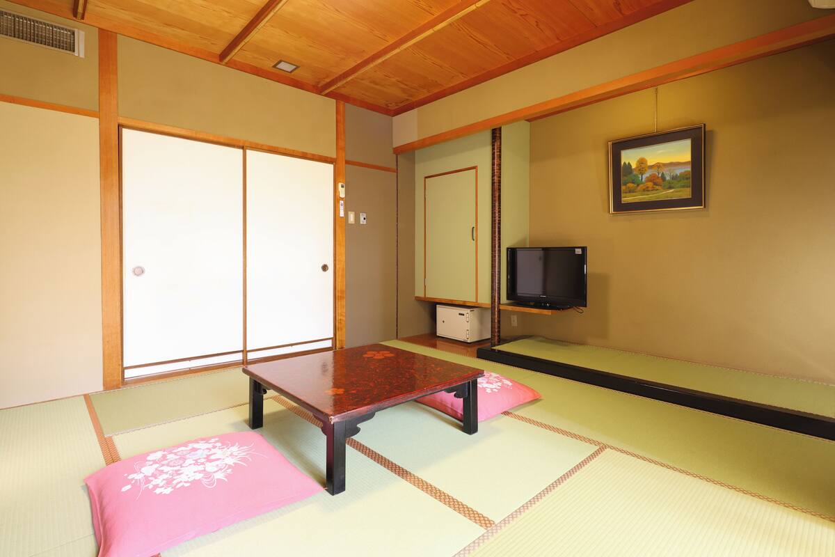 A traditional Japanese room with tatami flooring, a low wooden table, and a television on a shelf.