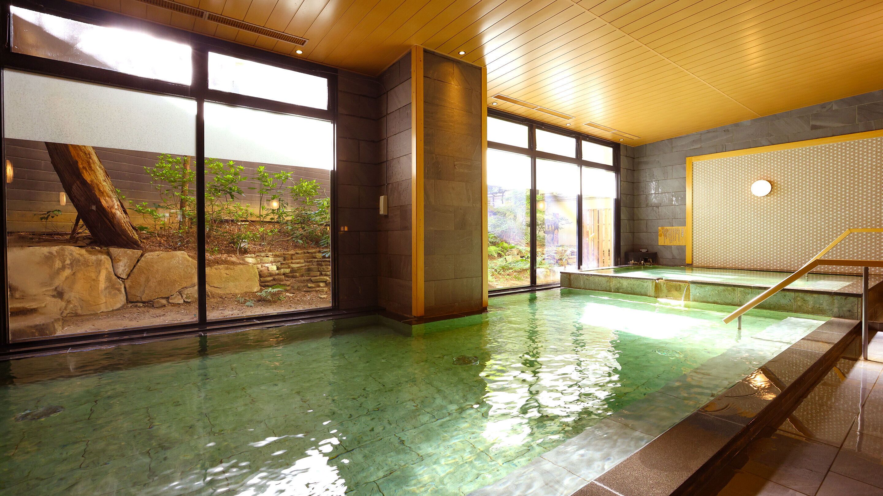Una grande piscina interna con acqua cristallina, travi in legno a soffitto e vista su un giardino esterno.