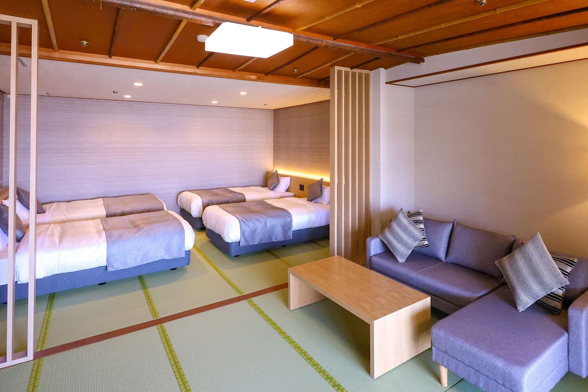 A hotel room with two beds, a sofa, a coffee table, and a floor lamp.