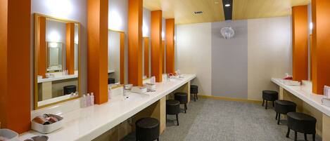 Una fila di lavabi con specchi e articoli da toilette, una ventola a soffitto e sgabelli in vimini.