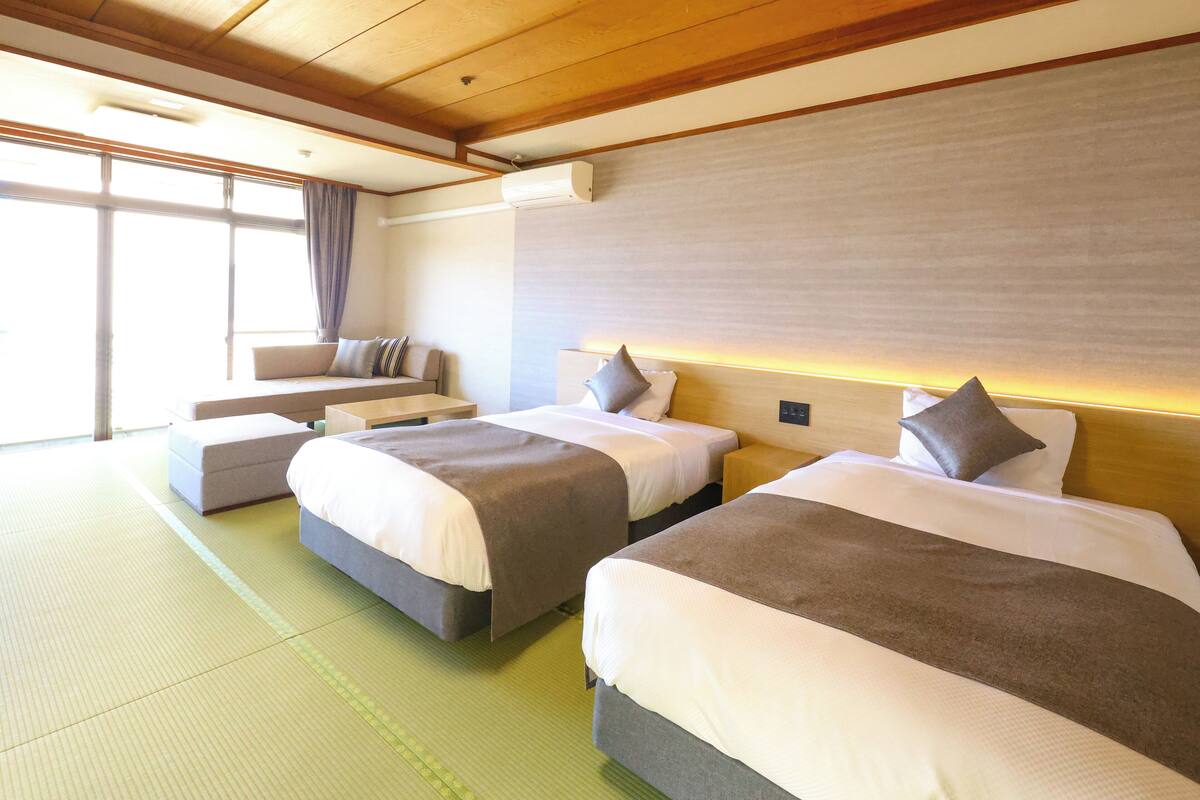 A hotel room with two beds, a sofa, and a large window.