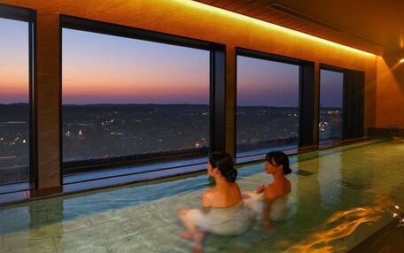 A large indoor swimming pool with a view of a cityscape at dusk.