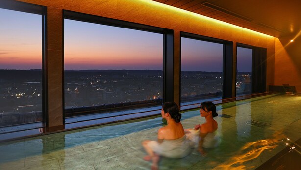 A large indoor swimming pool with a view of a cityscape at dusk. - Ooedo Onsen Monogatari Premium Yamashitaya (Kaga)
