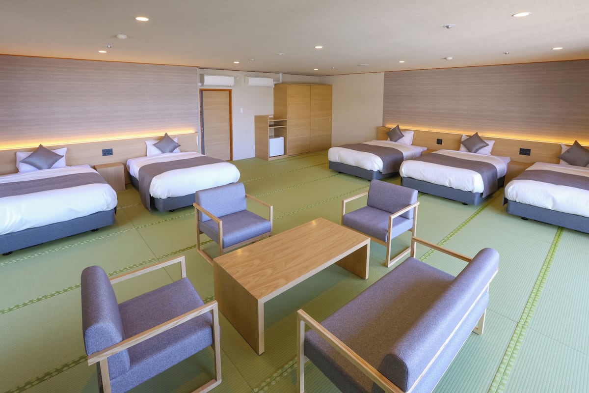 A hotel room with four beds, a seating area with chairs and a table, and a wardrobe.