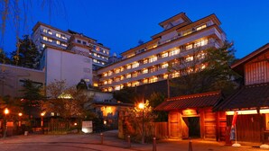A multi-story hotel with a traditional architectural style, featuring balconies and a courtyard with a wooden building. - Ooedo Onsen Monogatari Premium Yamashitaya (Kaga)