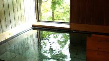 A room with a glass-bottomed pool reflecting trees, wooden walls, and a window.