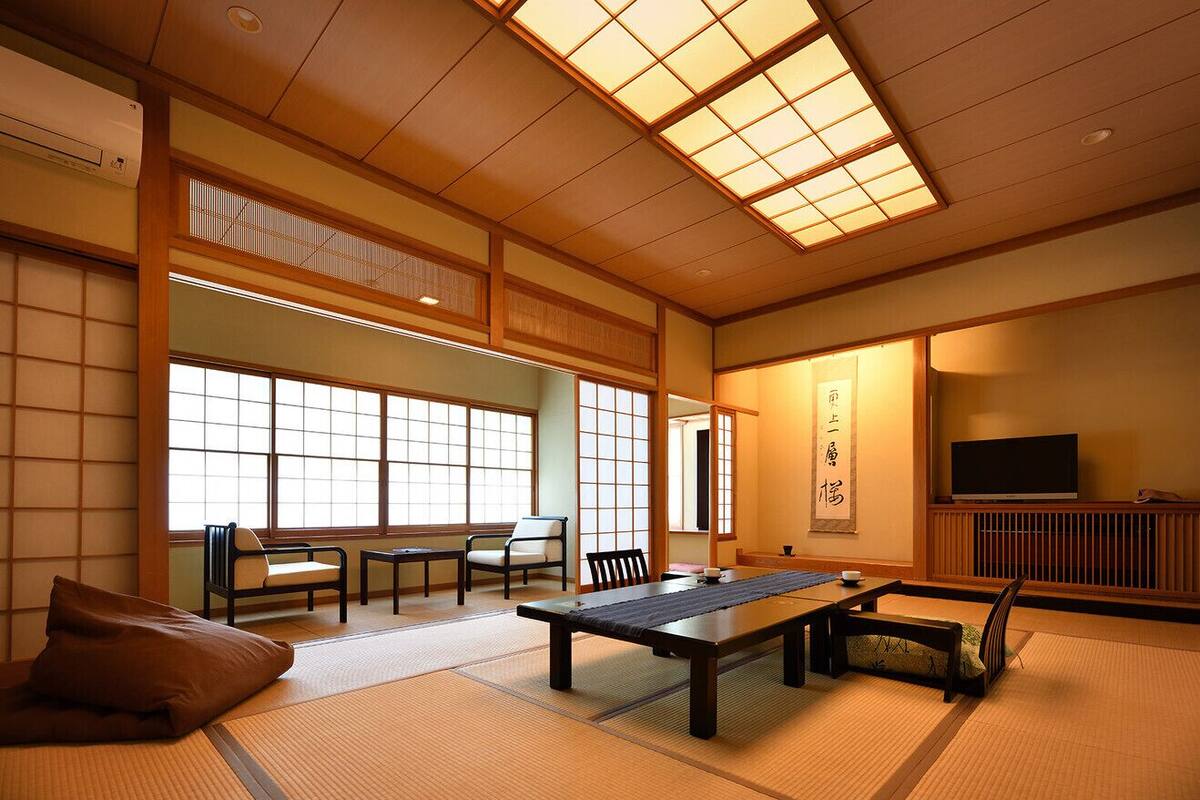 A traditional Japanese room with tatami flooring, a low table, chairs, a television, and a sliding door.