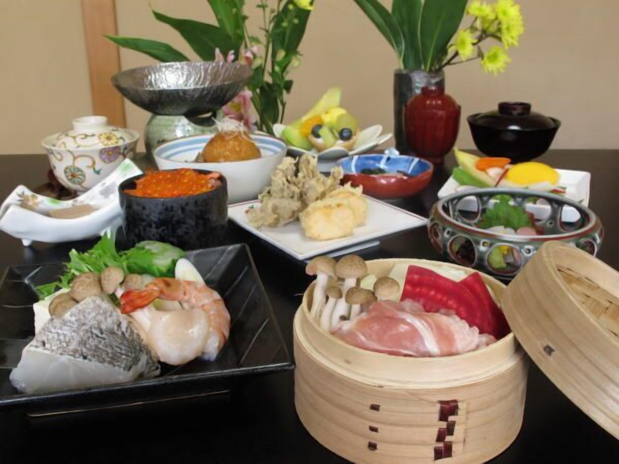 Forskellige retter på et bord, heriblandt sushi, sashimi og en dampkoger med kød.