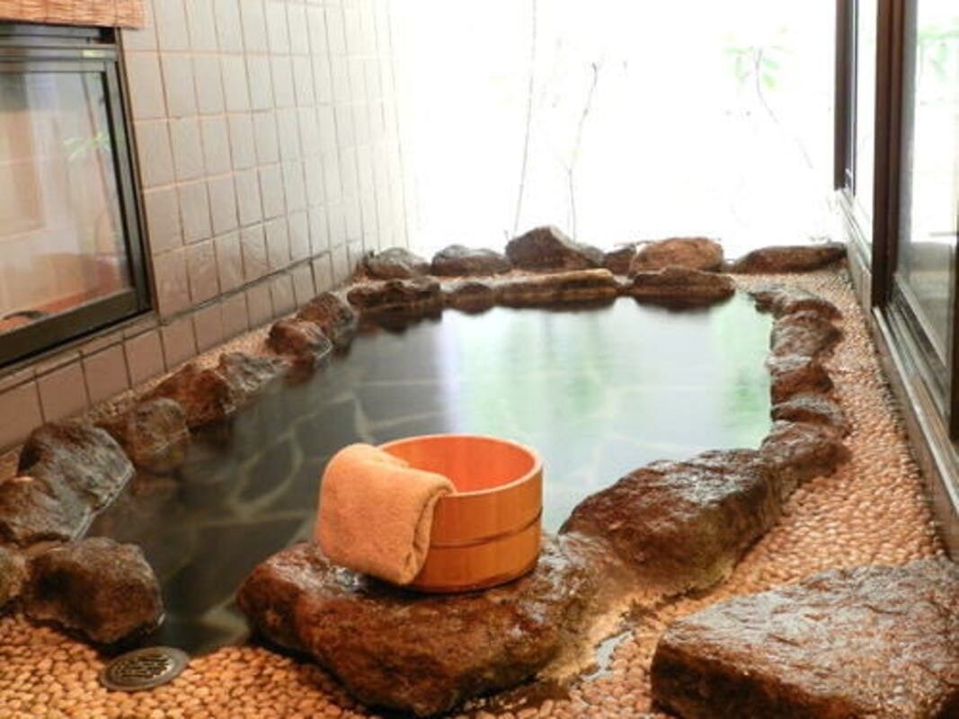 A hot spring bath with a wooden bench and a towel, surrounded by rocks.