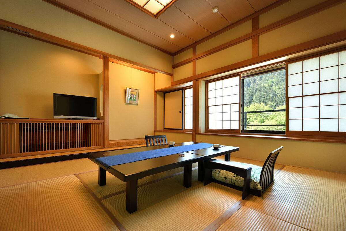 A traditional Japanese room with tatami flooring, a low table, a television, and large windows.