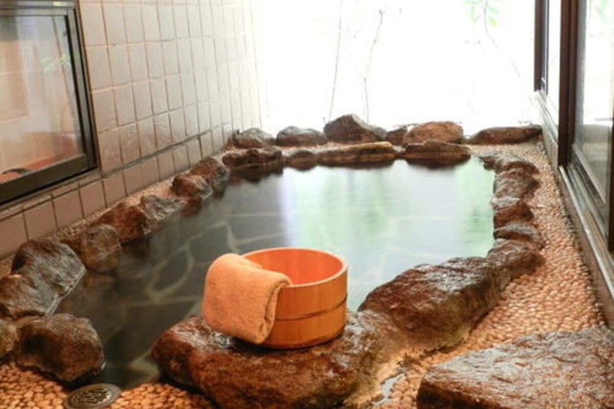 A hot spring bath with a wooden bench and a towel, surrounded by rocks.