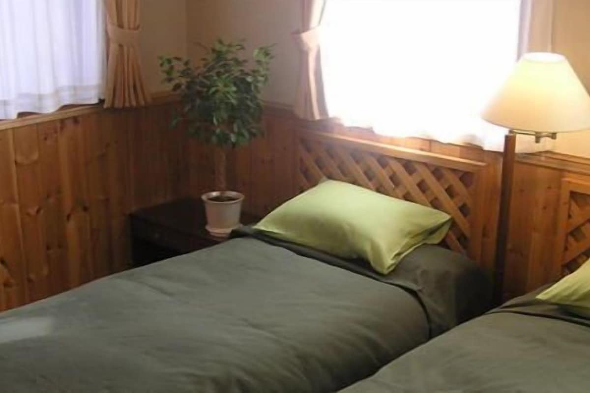 A room with two single beds, a wooden headboard, a bedside table with a lamp, and a window with curtains.