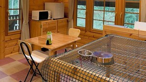 A wooden cabin with a dining table, chairs, a microwave, and a pet cage. - Plaisir (Suzaka)