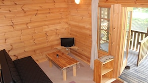 A wooden cabin interior with a sofa, a table with a TV, and a balcony with a railing. - Plaisir (Suzaka)