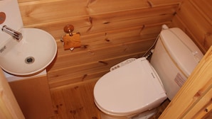 A wooden cabin bathroom with a sink, toilet, and wooden wall paneling. - Plaisir (Suzaka)