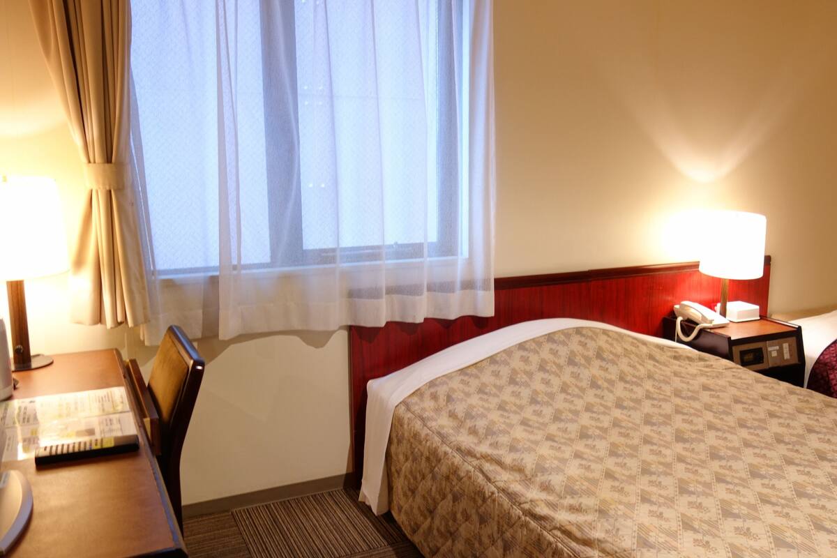 A hotel room with a bed, a desk, a telephone, and a window with curtains.