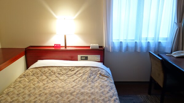 A hotel room with a bed, a bedside table with a lamp, a digital clock, and a telephone.