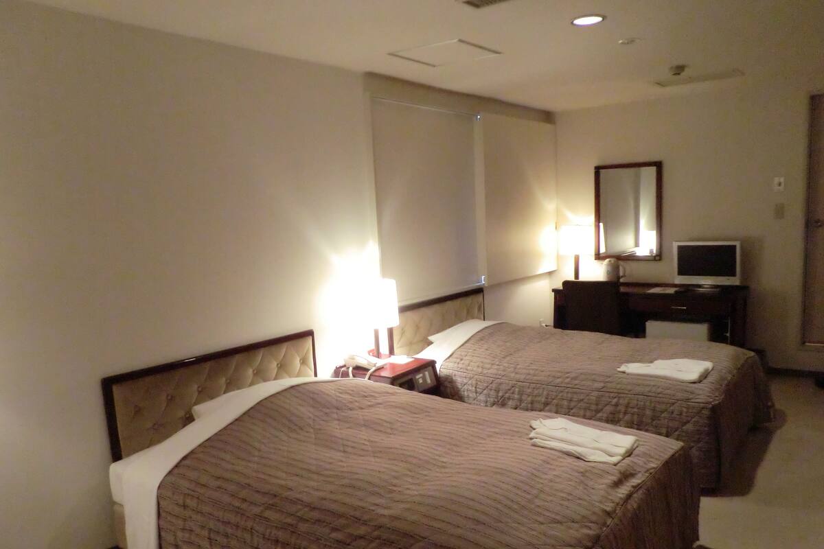 A hotel room with two beds, a desk with a computer, a lamp, and a mirror on the wall.