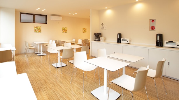A modern dining area with white tables and chairs, a coffee station, and artwork on the walls. - Hotel Green Park (Sendai)