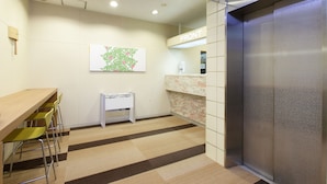 A modern elevator with a control panel, a wall-mounted sign indicating the front, and a small table with chairs in a hallway. - Hotel Green Park (Sendai)