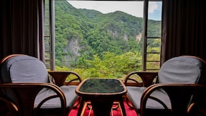 A room with two wicker chairs and a small table, overlooking a lush green valley with mountains. - Goroukaku (Numata)