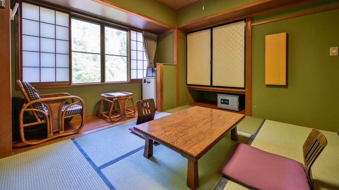 Una habitación japonesa tradicional con suelo de tatami, una mesa baja de madera y una zona de estar con otra mesa baja y sillas.