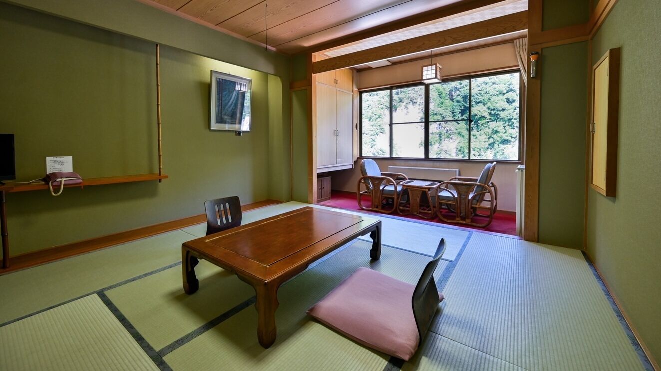 Una habitación tradicional de tatami con una mesa de madera, esteras de tatami, una ventana que ofrece vistas a árboles y un bajo techo de madera.