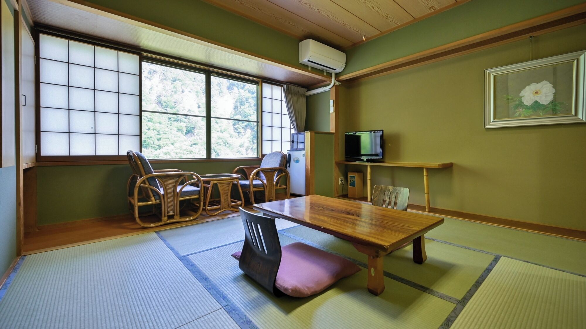 Habitación con tatami, una mesa de madera, sillas, un televisor y ventana con vista a árboles.