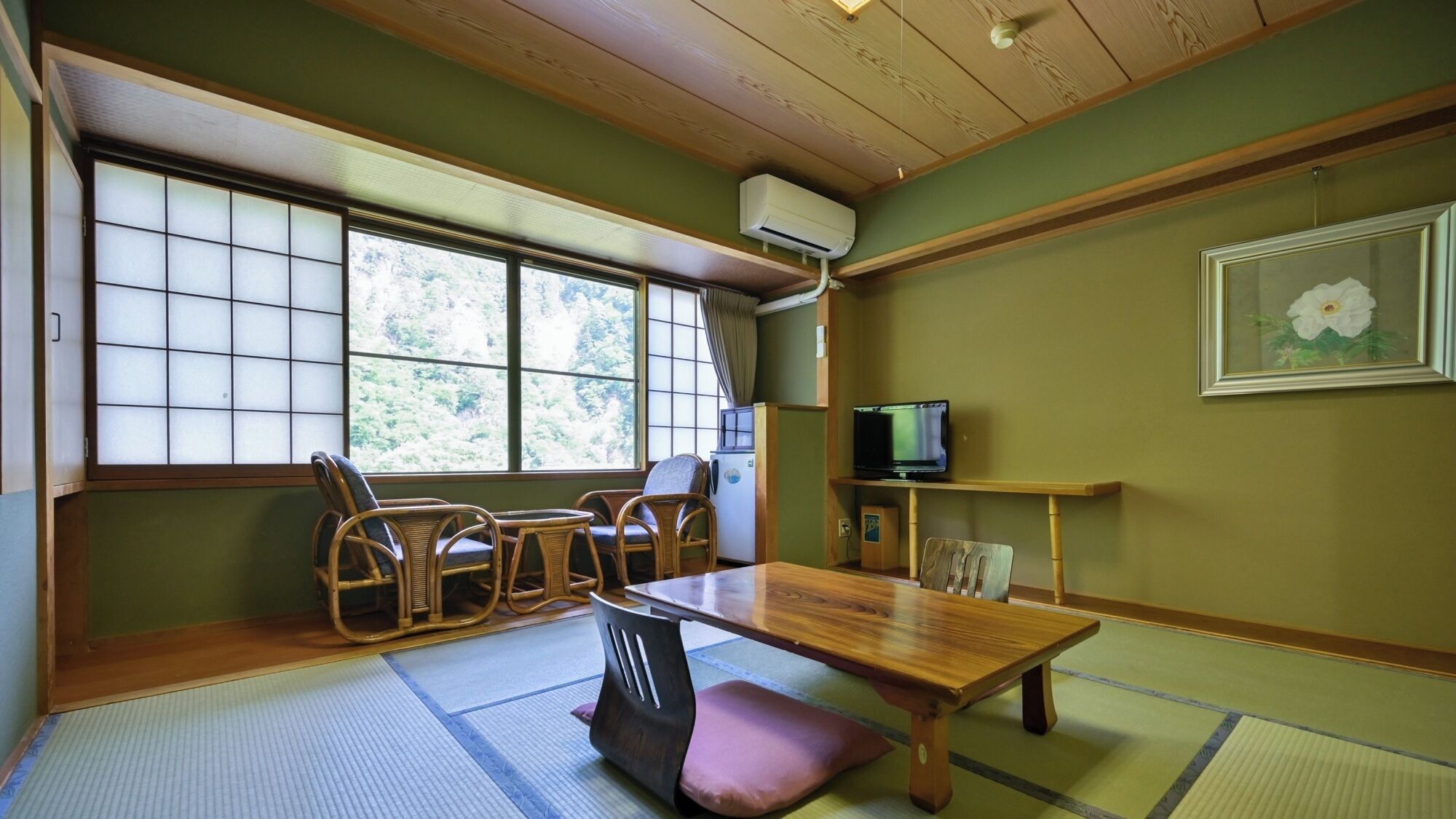 Una habitación japonesa tradicional con suelo de tatami, una mesa baja y un televisor sobre una estantería.