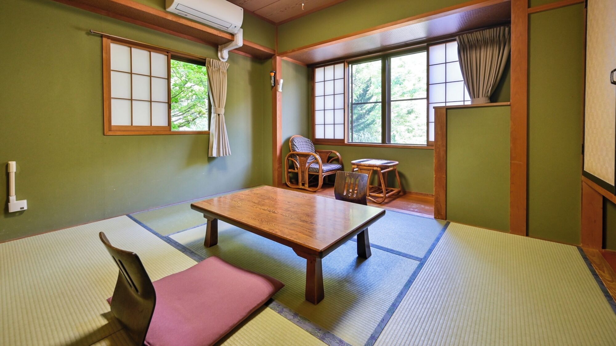 Una habitación con esteras de tatami, una mesa de madera, sillas y vistas a zonas verdes al exterior.
