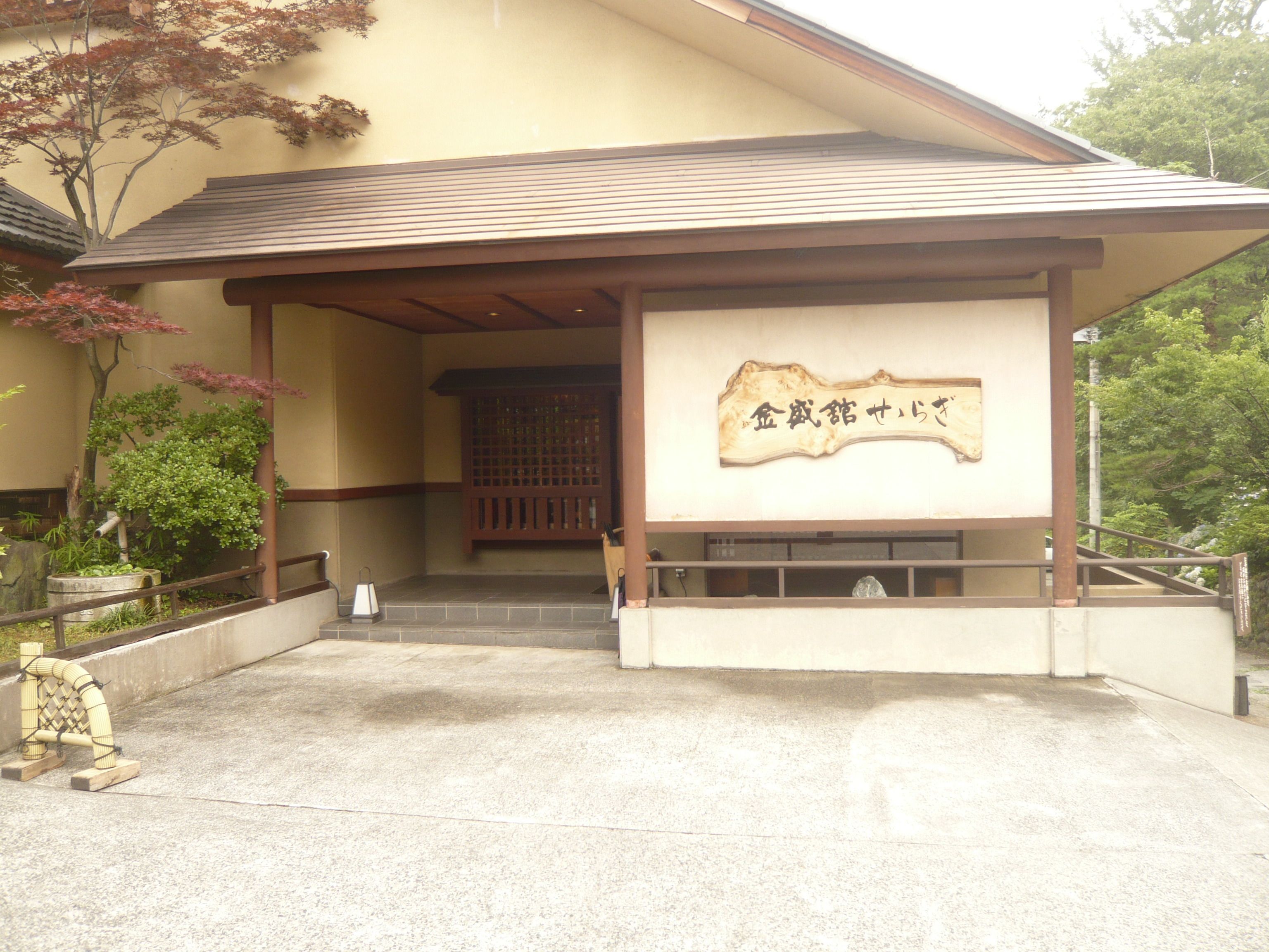 A building entrance with a covered porch, a stone lantern, and a wooden sign with Japanese characters.