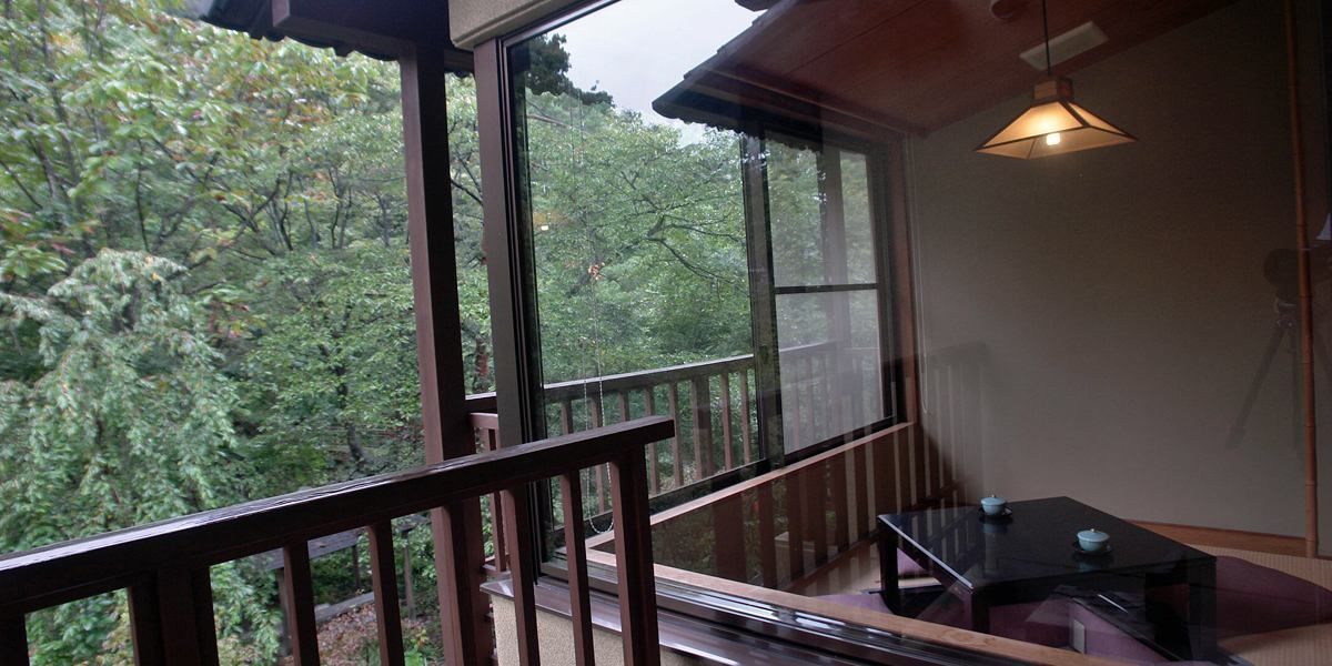 A balcony with a view of dense trees, a wooden railing, and a table with a teapot.