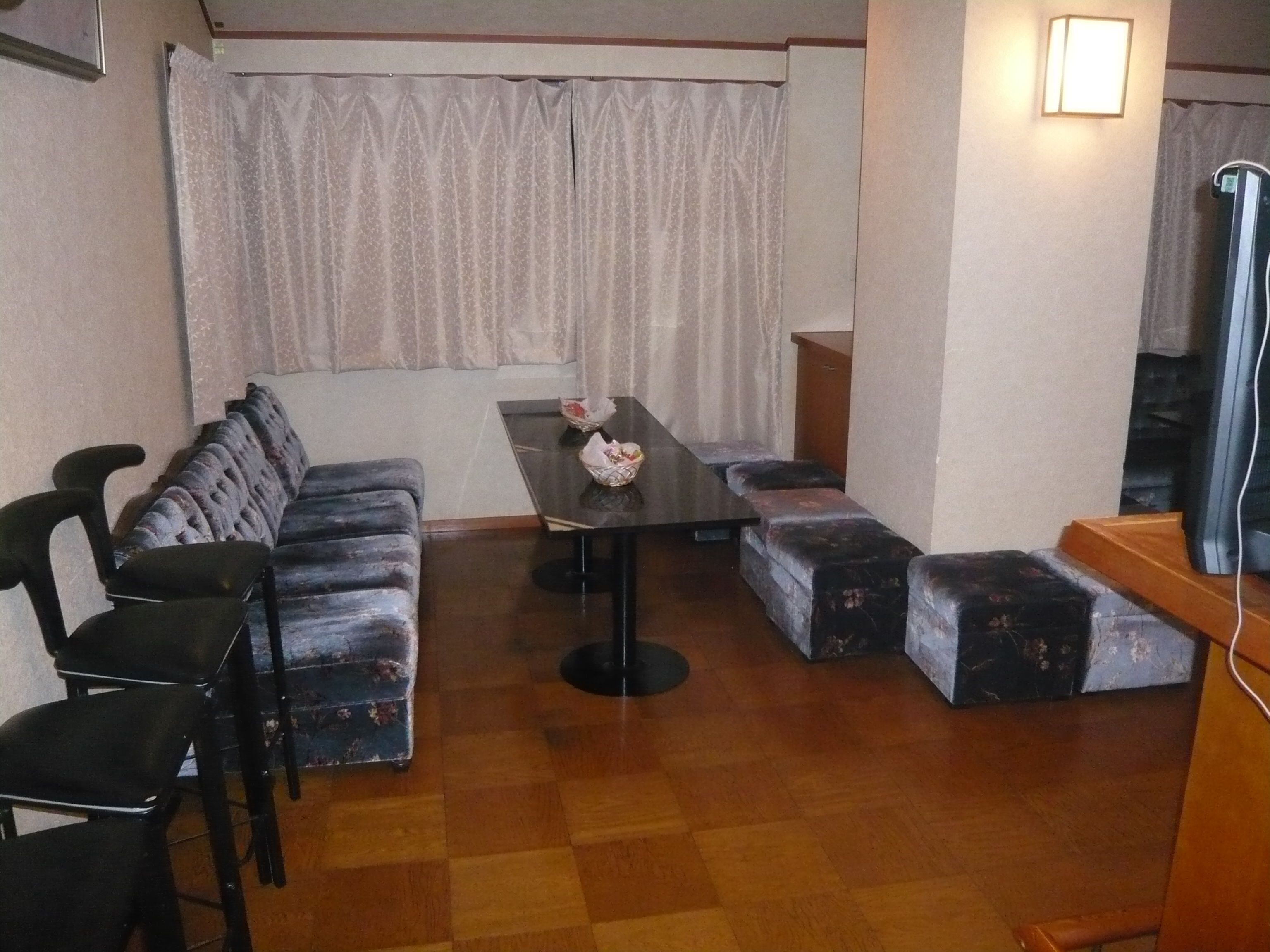 A room with a sofa, two armchairs, a small table with tissues, and a television on a wooden stand.