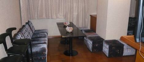 A room with a sofa, two armchairs, a small table with tissues, and a television on a wooden stand.