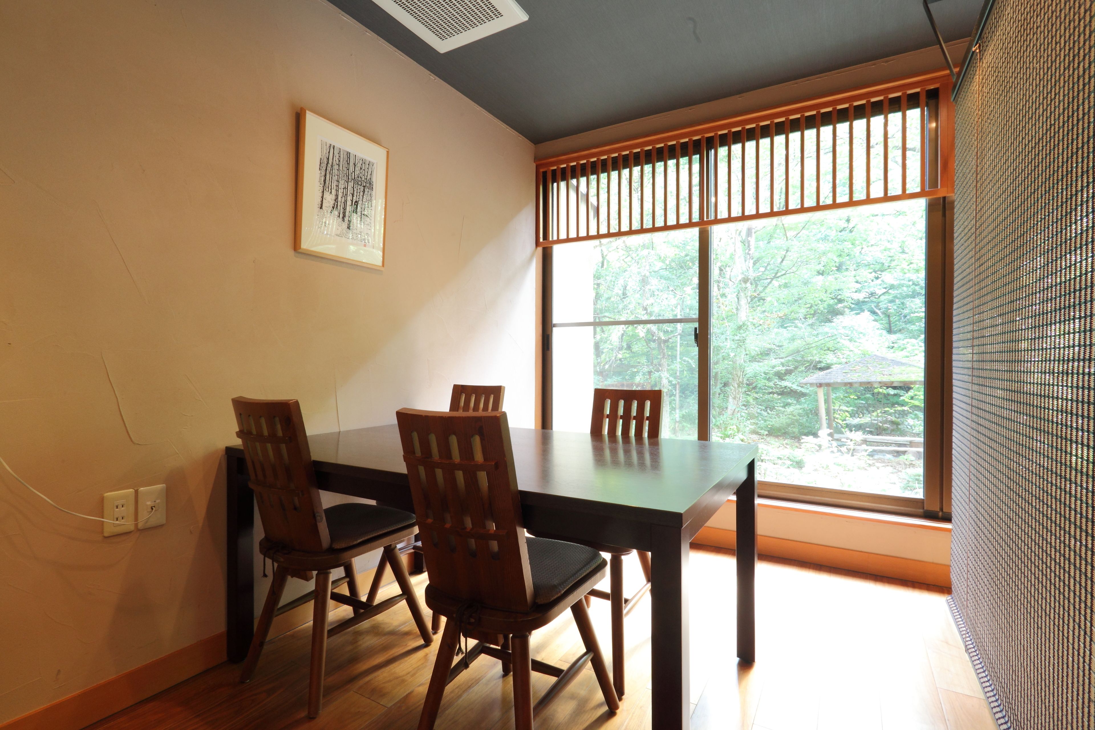 A dining area with a table and four chairs, a window with blinds, and a wall-mounted electrical outlet.