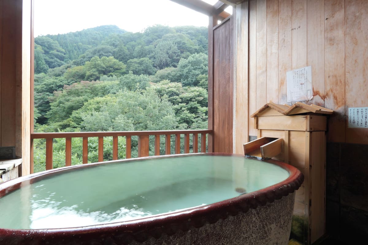 A traditional wooden bath with a view of a forested hillside.