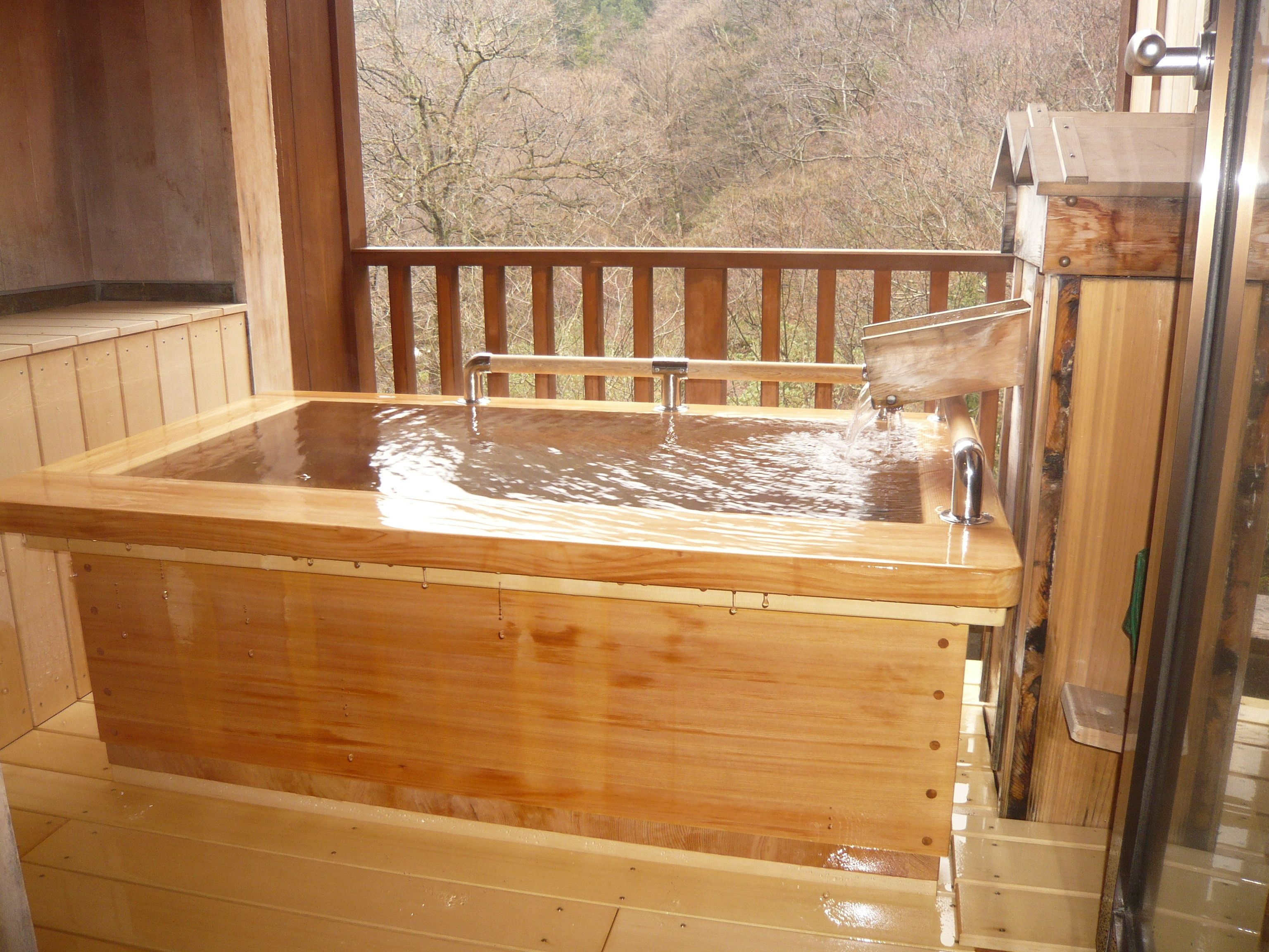 Una bañera de hidromasaje de madera con llave metálica y baranda de madera.
