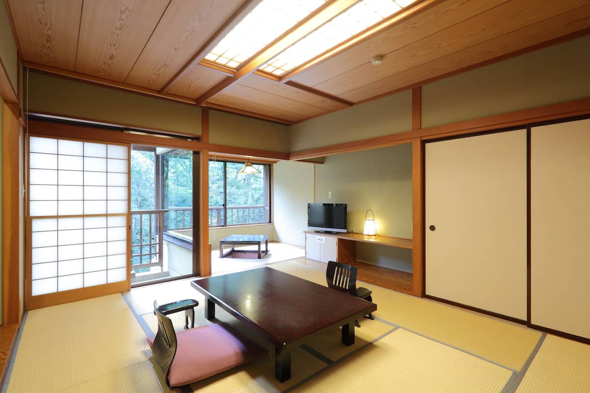 A traditional Japanese room with tatami flooring, a low table, a bench, sliding doors, and a television.