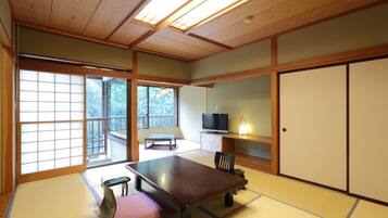 A traditional Japanese room with tatami flooring, a low table, a bench, sliding doors, and a television.