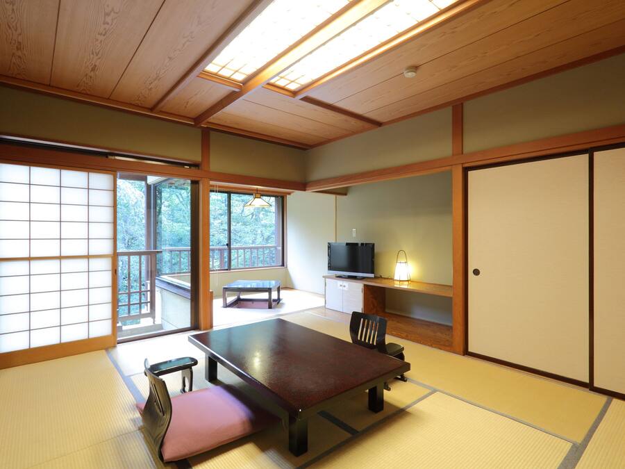 A traditional Japanese room with tatami flooring, a low table, a bench, sliding doors, and a television.