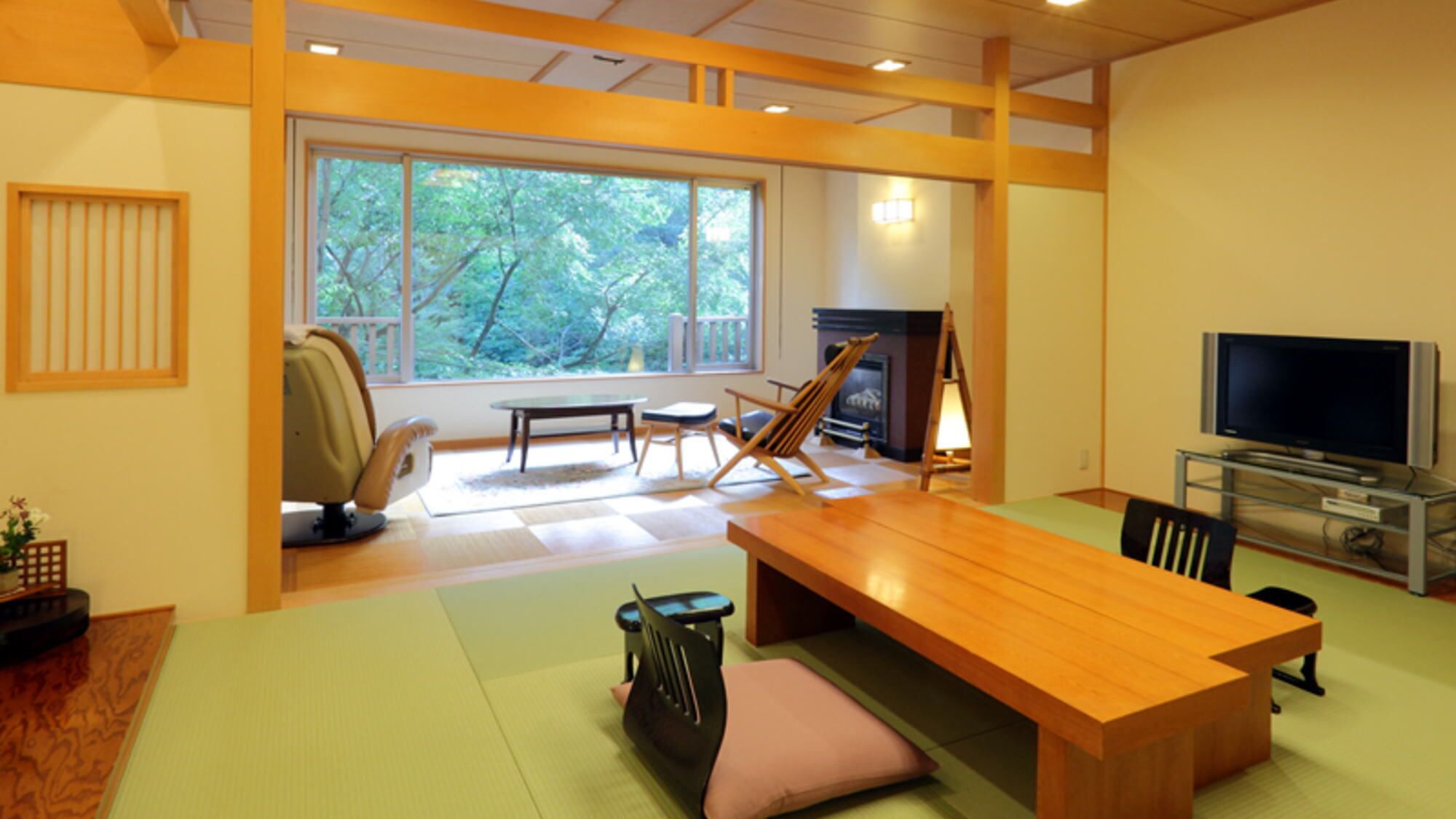 Una sala de estar moderna con una mesa de madera, sillas, un sofá, una chimenea, un televisor y ventanas amplias con vistas a árboles.