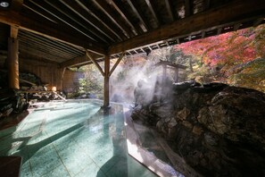 Un onsen japonés tradicional con una bañera de piedra, vigas de madera y vistas a follaje otoñal colorido.
