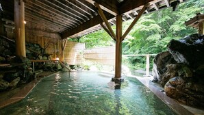 Un onsen japonés tradicional con estructura de madera, agua cristalina y entorno natural.