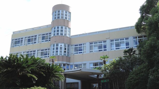 Un edificio de varios pisos con una torre central, ventanas grandes y una zona de entrada cubierta.