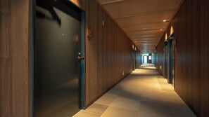 Un long couloir étroit aux murs et aux portes en bois, qui mène à une sortie lumineuse au bout.