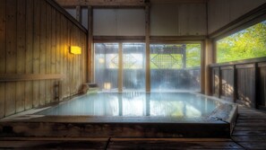 Baño de aguas termales con paredes de madera y vista a los árboles.